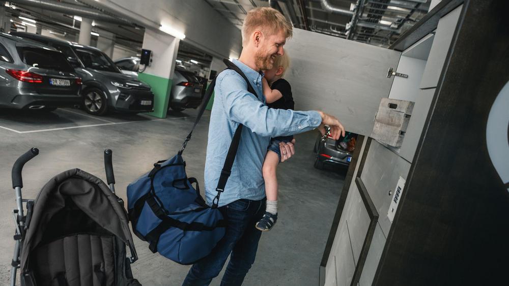 Ung far med barn på armen henter ut pakke fra pakkesentral i garasjeanlegg.
